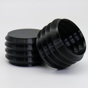 May include: Two black, cylindrical objects with a ridged design. One is upright, and the other is lying on its side. The objects have a textured top surface and are set against a white background.