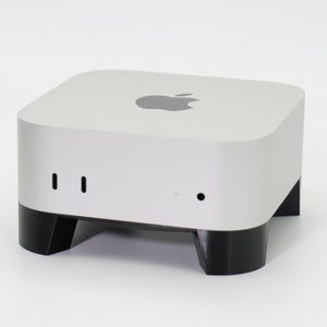 Peut inclure: Un ordinateur Apple Mac mini blanc avec des pieds noirs. L'ordinateur a un logo Apple argenté sur le dessus.