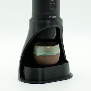 May include: A black Outlin coffee maker with a ceramic cup sitting on the base. The coffee maker has a clear lid and a digital display.