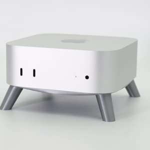 May include: A silver computer with a square shape and four legs. The computer has a small black dot and two small black lines on the front.