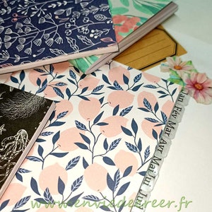 Peut inclure: Une pile de quatre petits carnets avec des couvertures à motifs différents. Le carnet du dessus a une couverture bleu marine avec un motif floral blanc. Le deuxième carnet a un motif floral vert et rose. Le troisième carnet a un fond blanc avec des citrons roses et des feuilles bleu foncé. Le quatrième carnet a un motif noir et blanc de créatures marines. Les carnets ont des languettes sur le côté avec les mois de l'année écrits dessus : Jan, Fev, Mar, Avr, Mai, Jun, Jul.