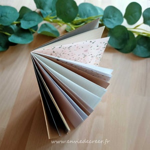 Peut inclure: Une pile de papier avec des pages de différentes couleurs, dont une page avec un motif terrazzo. Le papier est plié en deux et les pages sont étalées. Le texte "www.enviedecreer.fr" est visible en bas de l'image.