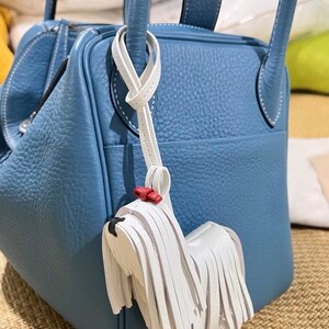 May include: A blue leather handbag with a white leather dog charm. The dog charm has a red bow and white fringe.