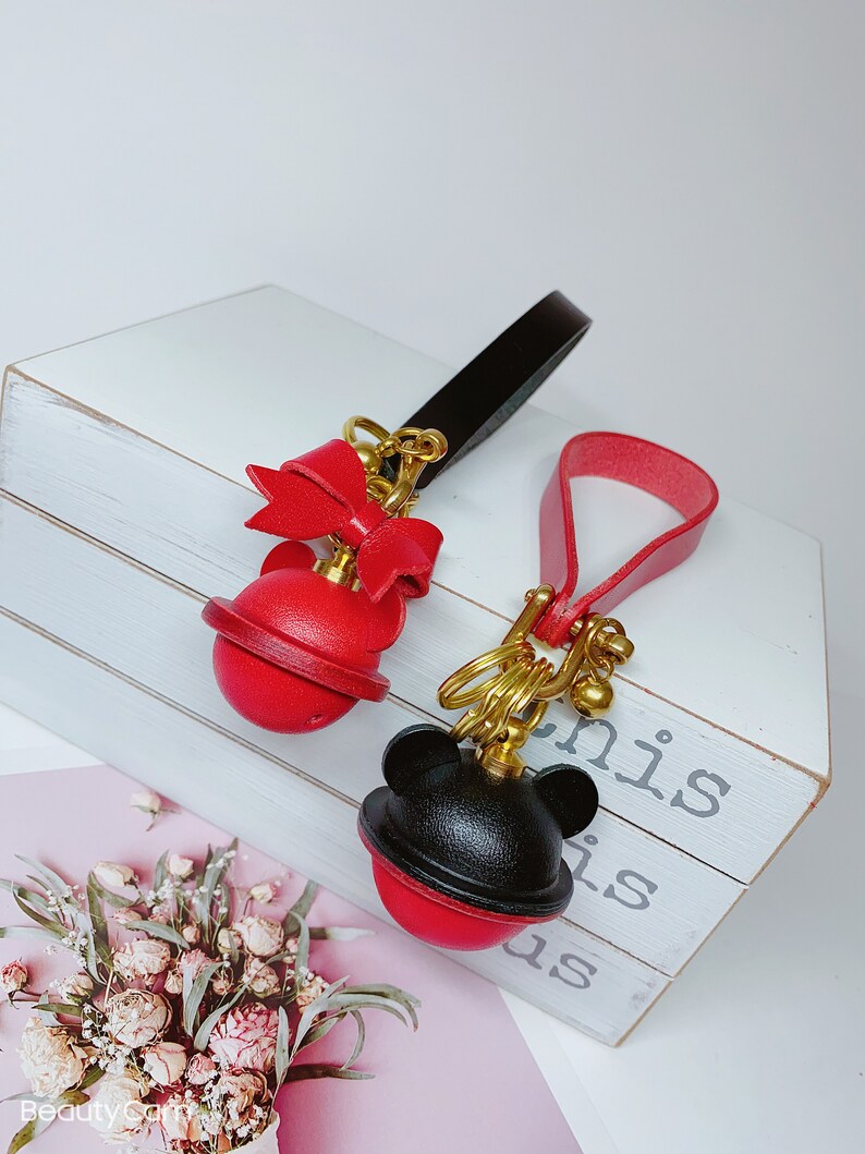 May include: Two leather keychains with red and black round charms. One charm has a red bow and the other has black mouse ears. Both charms have a gold metal ring and a gold metal bell.