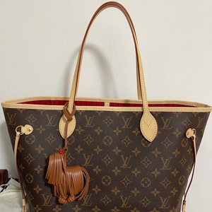 May include: A brown and tan Louis Vuitton tote bag with a red and white lining. The bag has a brown leather tassel attached to the handle.