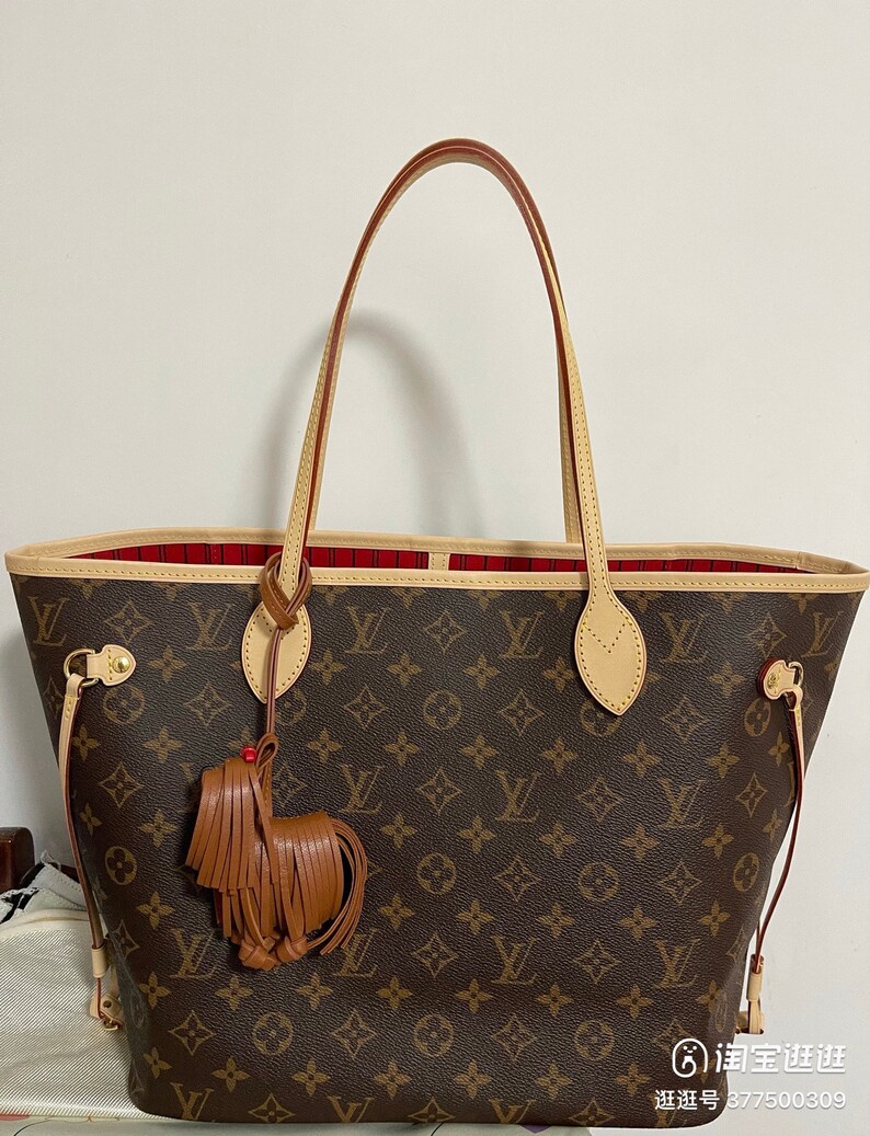 May include: A brown and tan Louis Vuitton tote bag with a red and white lining. The bag has a brown leather tassel attached to the handle.