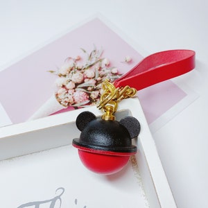May include: A red and black leather keychain with a Mickey Mouse head design. The keychain has a gold chain and a red leather strap.