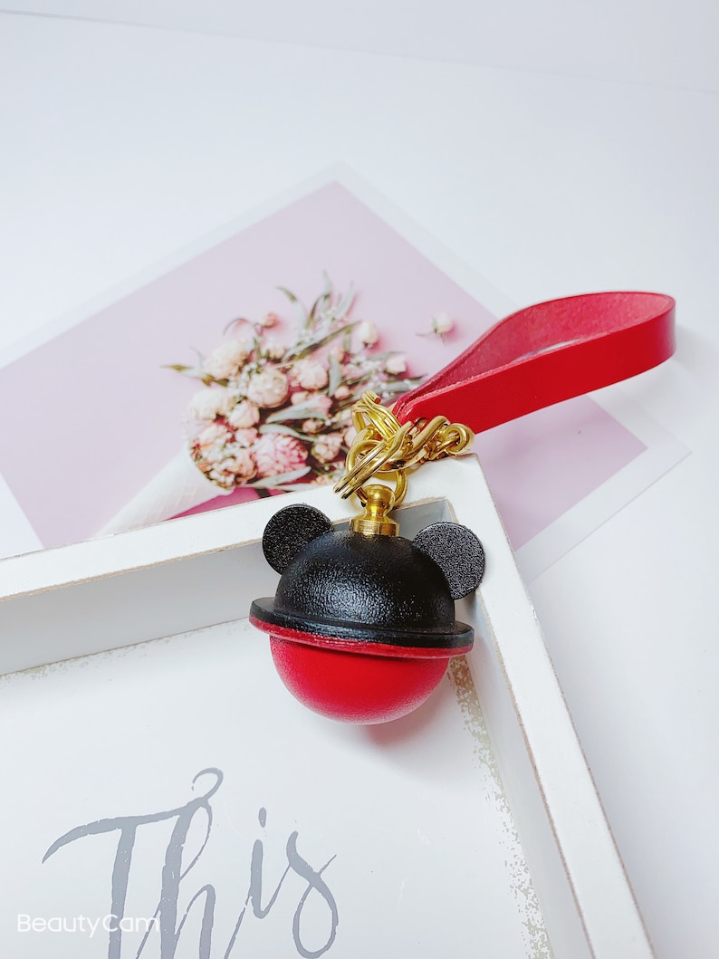 May include: A red and black leather keychain with a Mickey Mouse head design. The keychain has a gold chain and a red leather strap.