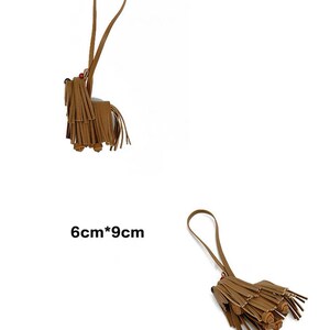 May include: A brown leather tassel keychain shaped like a dog with a 6cm by 9cm measurement. The keychain has a long brown strap.