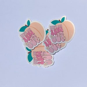 May include: A set of four peach-colored stickers with the text "Suns Out Buns Out" in pink and white lettering. The stickers feature a peach with a green leaf and pink flowers.