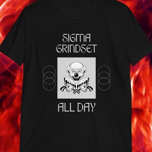 May include: Black t-shirt with a white graphic design. The graphic features a clown with a menacing expression holding two pistols. The text "SIGMA GRINDSET ALL DAY" is printed on the shirt.