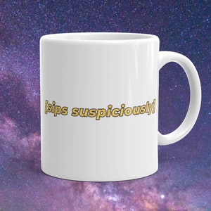 Puede incluir: Taza de cerámica blanca con un gráfico amarillo y naranja que dice "[sips suspiciously]"