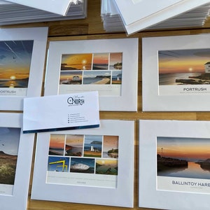 Puede incluir: Una colecci&oacute;n de impresiones enmarcadas que muestran paisajes pintorescos de la costa de Irlanda del Norte. Las impresiones se muestran sobre una superficie de madera e incluyen im&aacute;genes de Porttrush, Slemish, Ballintoy Harbour y otros lugares. Las impresiones est&aacute;n todas en marcos blancos con un passe-partout blanco.