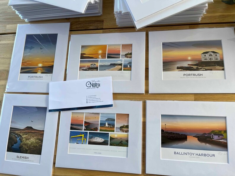 Puede incluir: Una colecci&oacute;n de impresiones enmarcadas que muestran paisajes pintorescos de la costa de Irlanda del Norte. Las impresiones se muestran sobre una superficie de madera e incluyen im&aacute;genes de Porttrush, Slemish, Ballintoy Harbour y otros lugares. Las impresiones est&aacute;n todas en marcos blancos con un passe-partout blanco.
