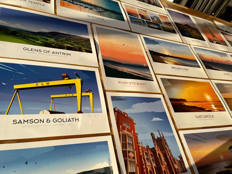 Puede incluir: Una colecci&oacute;n de impresiones ilustradas coloridas que representan varios monumentos y escenas de Irlanda del Norte. Las impresiones se muestran en una superficie de madera e incluyen lugares como Glens of Antrim, Samson & Goliath, Portstewart, Brown's Bay y Castlerock.