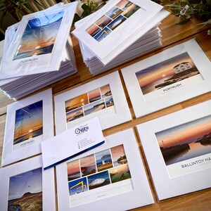 Puede incluir: Una colecci&oacute;n de impresiones enmarcadas que muestran paisajes pintorescos de la costa de Irlanda del Norte. Las impresiones se muestran en una mesa de madera e incluyen im&aacute;genes de Porttrush y Ballintoy Harbour. Las impresiones est&aacute;n todas en marcos blancos con un passe-partout blanco.