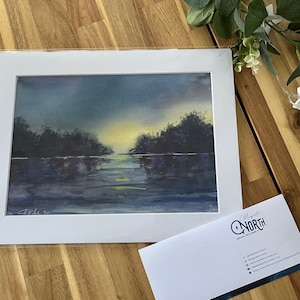 Puede incluir: Una pintura de acuarela en un paspartú blanco que muestra un cielo crepuscular azul oscuro y morado sobre un cuerpo de agua tranquilo con árboles en silueta y un sol amarillo brillante en el horizonte. Una tarjeta de visita con el texto Magnetic North.