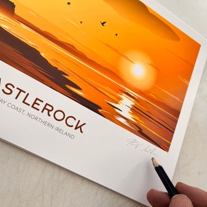 Puede incluir: Una ilustraci&oacute;n colorida de una puesta de sol sobre el oc&eacute;ano con un acantilado rocoso en la distancia. El texto "CASTLEROCK" est&aacute; impreso en letras marrones con las palabras "CAUSEWAY COAST, NORTHERN IRELAND" impresas debajo.