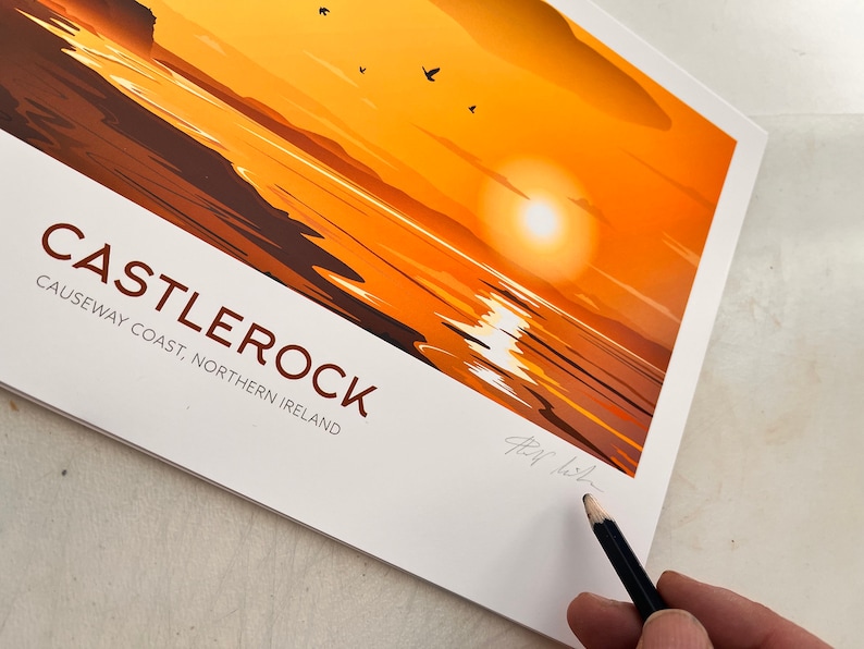 Puede incluir: Una ilustraci&oacute;n colorida de una puesta de sol sobre el oc&eacute;ano con un acantilado rocoso en la distancia. El texto "CASTLEROCK" est&aacute; impreso en letras marrones con las palabras "CAUSEWAY COAST, NORTHERN IRELAND" impresas debajo.