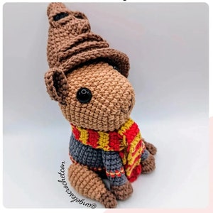 May include: A brown crocheted stuffed animal wearing a brown crocheted Sorting Hat, a gray crocheted sweater, and a red and yellow striped scarf.