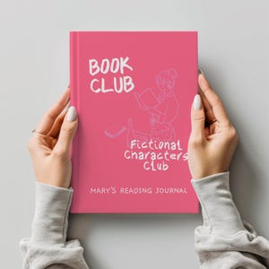 Puede incluir: Un libro rosa con las palabras "BOOK CLUB" en blanco, junto con una ilustración de una persona leyendo. También se ve el texto "Fictional Characters Club" y "MARY'S READING JOURNAL". El libro lo sostiene una persona.