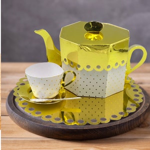 Può includere: Un set da tè in oro con pois bianchi. La teiera ha un coperchio e un manico. La tazza ha un piattino. Il set è su un sottobicchiere oro e bianco a pois.