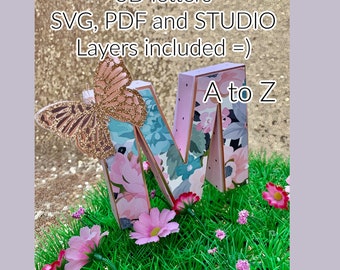 May include: A 3D letter M with a floral design, a butterfly, and the text "A to Z". The letter is sitting on a bed of green grass with pink flowers.