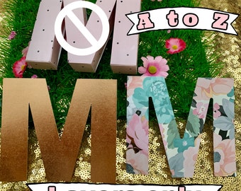 以下が含まれることがあります： 異なるスタイルで「MMM」と綴られた3つのペーパークラフトレター。最初のレターは、黒い水玉模様と斜めの線が引かれたピンク色。2番目のレターは、グラデーションがかかった金色。3番目のレターは、花柄の白色。レターは、ゴールドのグリッター背景に、「Layers only」と書かれたピンクの横断幕と、「A to Z」と書かれたピンクの横断幕が置かれています。