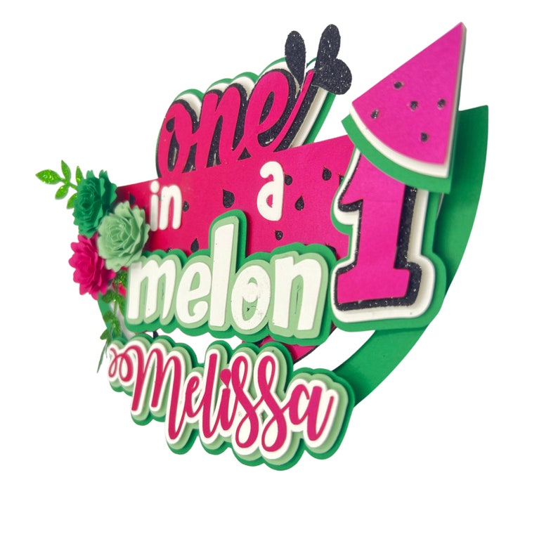 May include: A pink and green watermelon-themed cake topper with the text "one in a melon" and the number "1" in pink with glitter. The name "Melissa" is written in pink with a green outline.