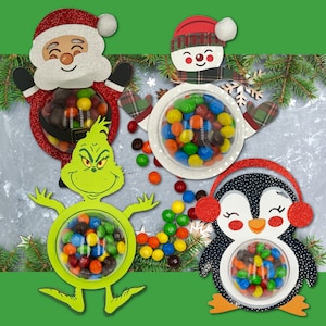 Könnte beinhalten: Vier festliche Süßigkeitenhalter in Form von Weihnachtsmann, Schneemann, Grinch und Pinguin. Jede Figur hat einen transparenten, runden Behälter, der mit bunten Süßigkeiten gefüllt ist. Der Weihnachtsmann und der Pinguin haben rote Glitzerakzente.