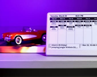 May include: A digital tablet displaying a schedule for Saturday, March 29, with various appointments. A red toy car and a stack of books are visible in the background. The tablet shows the time as 08:01 PM.