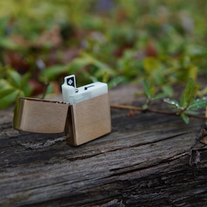 May include: A silver lighter with a black and white design. The lighter is open and the lid is flipped back. The lighter is sitting on a wooden surface.