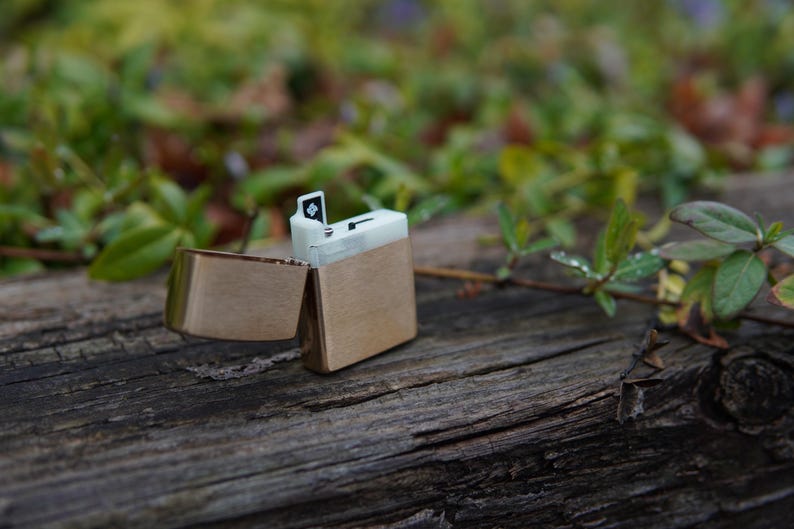 May include: A silver lighter with a black and white design. The lighter is open and the lid is flipped back. The lighter is sitting on a wooden surface.