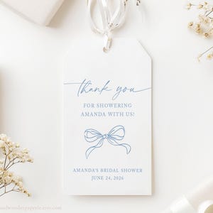 May include: White gift tag with blue text that reads "Thank you for showering Amanda with us!" and "Amanda's Bridal Shower June 24, 2026." A blue bow illustration is below the text. The tag is tied with a white ribbon.