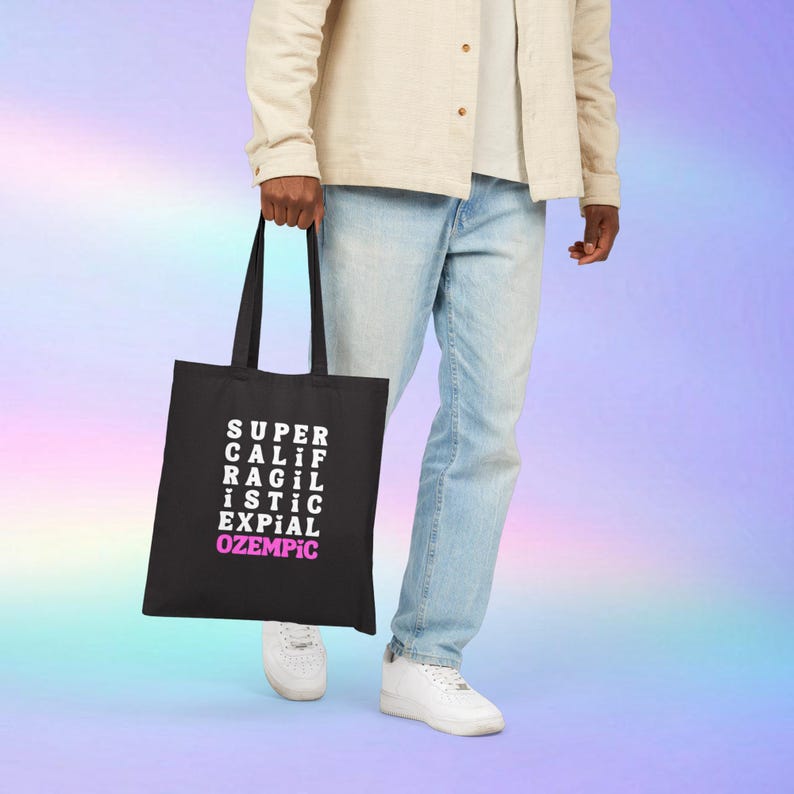 May include: A black tote bag with white text that reads "SUPER CALIF RAGIL ISTIC EXPIAL OZEMPIC" in a grid pattern. The text "OZEMPIC" is in pink.
