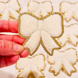 Puede incluir: Un conjunto de lazos de fieltro blanco con ribete de purpurina dorada. Los lazos son perfectos para agregar un toque de brillo a cualquier proyecto artesanal.