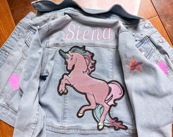 May include: A light blue denim jacket with a pink unicorn patch, a pink heart patch, a star patch, and the name "Siena" embroidered on the back.