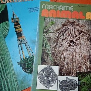 May include: Two vintage macrame books. One titled "Macrame Animal" with a lion illustration and the other "Amé Unlimited II". The books are on an orange surface. The "Macrame Animal" book has a green cover with orange text.