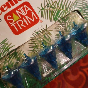May include: A package of blue Christmas tree ornaments. The package has the words "SANTA TRIM" in white letters on a red background. The ornaments are in a clear plastic package.