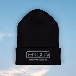 Pode incluir: Gorrinho preto com a palavra "ENCOM" num design retangular branco na frente. Abaixo da palavra "ENCOM" está o texto "ENCOM COMPUTER TECHNOLOGY CORP." em branco. O gorro está sobre um fundo de céu azul.
