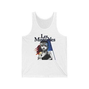 Puede incluir: Camiseta blanca de tirantes con un gráfico de una niña sosteniendo una bandera francesa. El texto "Les Misérables" está impreso sobre el gráfico.