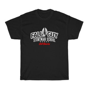 May include: Black t-shirt with a white graphic of a stylized eagle with the text "Fall Guy Stuntman School" and "Critt Seavers" in red.