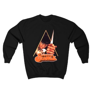 Op de afbeelding: Zwart sweatshirt met een grafische print van een man die een mes vasthoudt voor een driehoek. De tekst "Clockwork Orange" is in oranje onder de afbeelding gedrukt.