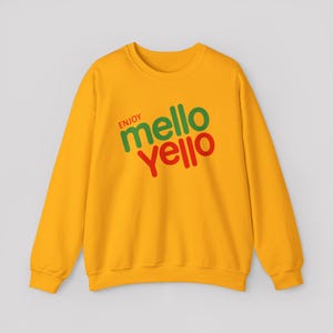 Peut inclure: Un sweat-shirt jaune vif à manches longues et col rond avec le texte "ENJOY mello YELLO" imprimé en diagonale sur la poitrine. Le mot "ENJOY" est en petites lettres rouges, "mello" est en vert et "YELLO" est en grandes lettres rouges.