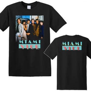 May include: A black short-sleeve t-shirt featuring a graphic print of the Miami Vice cast on the front and the text MIAMI VICE in teal and pink on both the front and back. The shirt has a crew neckline and a standard straight-cut silhouette.