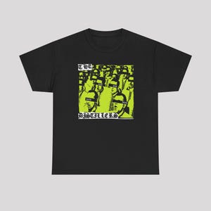 Pode incluir: Uma t-shirt preta de manga curta com uma impressão gráfica quadrada em verde lima e preto. O design retrata uma multidão de pessoas com barras pretas sobre os olhos e o texto THE DISTILLERS impresso numa fonte gótica ousada e estilizada.
