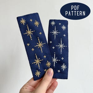 Op de afbeelding: Twee marineblauwe kruissteek bladwijzers met gouden en witte sterpatronen. De bladwijzers zijn rechthoekig en hebben verschillende sterontwerpen. Een marineblauw ovaal met de tekst "PDF PATTERN" staat op de achtergrond.