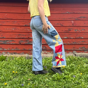 Peut inclure: Jean bleu clair avec des détails de patchwork sur le bas de la jambe. Le patchwork présente des formes géométriques rouges, jaunes et bleues. Le jean a une conception classique à cinq poches et une coupe droite.