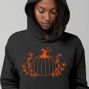 May include: A black hoodie with an orange outline of a pumpkin with leaves. The pumpkin has a stem and is surrounded by leaves.