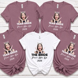 May include: Four mauve t-shirts and one white t-shirt featuring a custom photo print of a person wearing a crown, with the text TEAM BRIDE or THE BRIDE, Tina's Hen Do, and 2026 printed below the image on each garment.